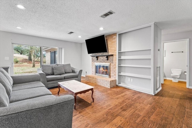 living room featuring wood-type flooring, built in features, a textured ceiling, and a fireplace