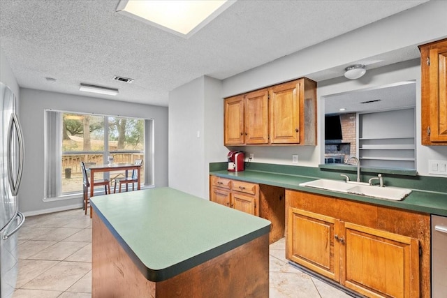 kitchen with light tile patterned flooring, appliances with stainless steel finishes, sink, a center island, and a textured ceiling