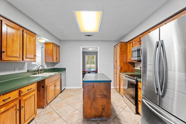 kitchen featuring sink, a textured ceiling, light tile patterned floors, appliances with stainless steel finishes, and a kitchen island