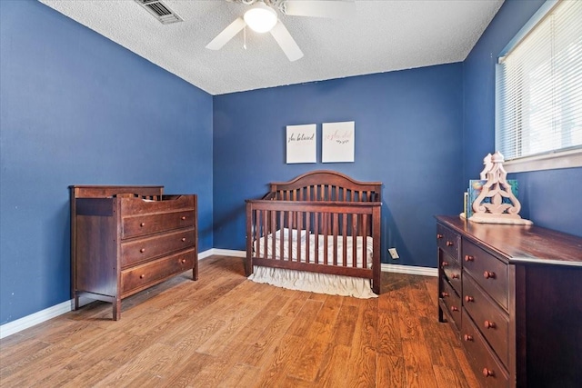 bedroom with ceiling fan, a nursery area, a textured ceiling, and light wood-type flooring