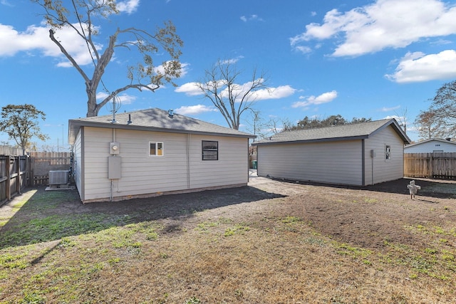 back of house featuring a fenced backyard, an outbuilding, central AC, and a yard