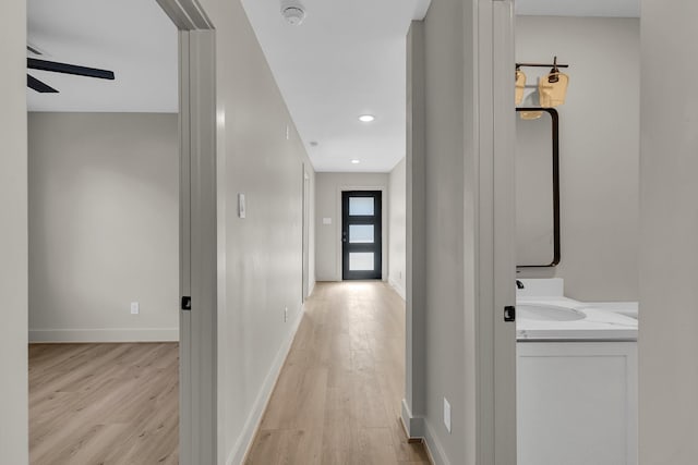 hall featuring light wood finished floors, recessed lighting, a sink, and baseboards