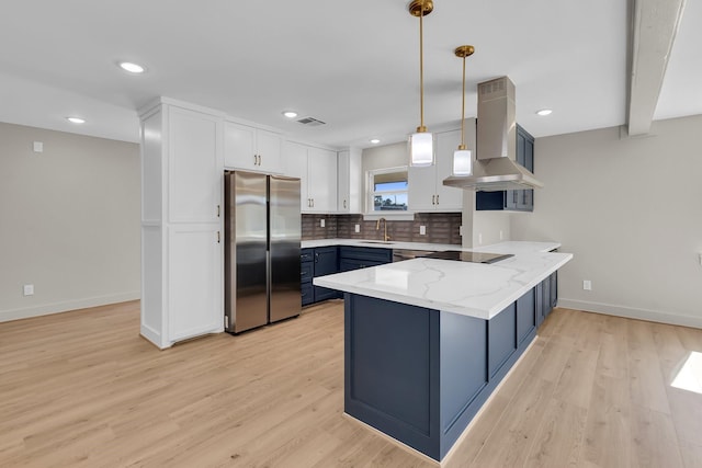 kitchen featuring island exhaust hood, freestanding refrigerator, white cabinetry, blue cabinets, and a peninsula