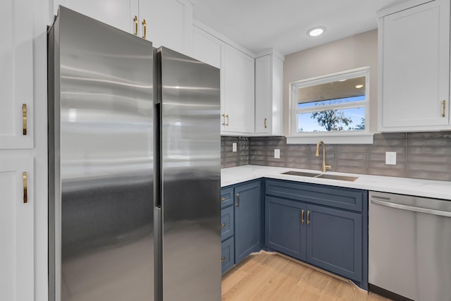 kitchen with stainless steel appliances, a sink, white cabinets, blue cabinetry, and tasteful backsplash