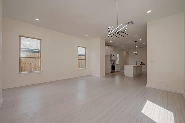 unfurnished living room with sink, a chandelier, and light hardwood / wood-style flooring