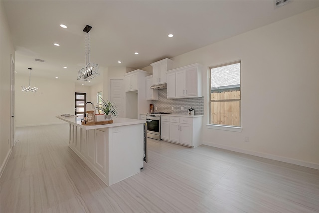 kitchen featuring a breakfast bar, stainless steel stove, tasteful backsplash, white cabinetry, and a kitchen island with sink