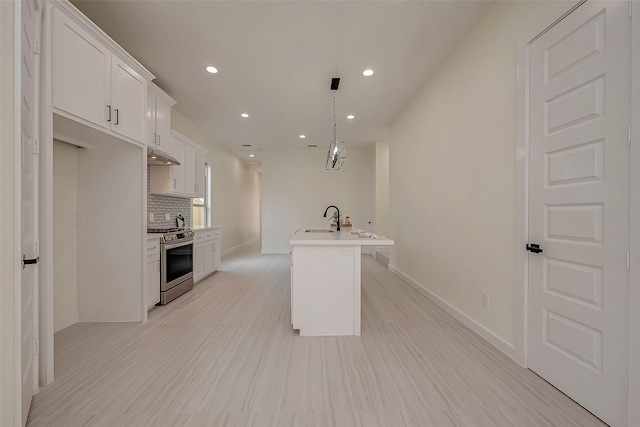 kitchen with stainless steel gas stove, an island with sink, sink, white cabinets, and backsplash