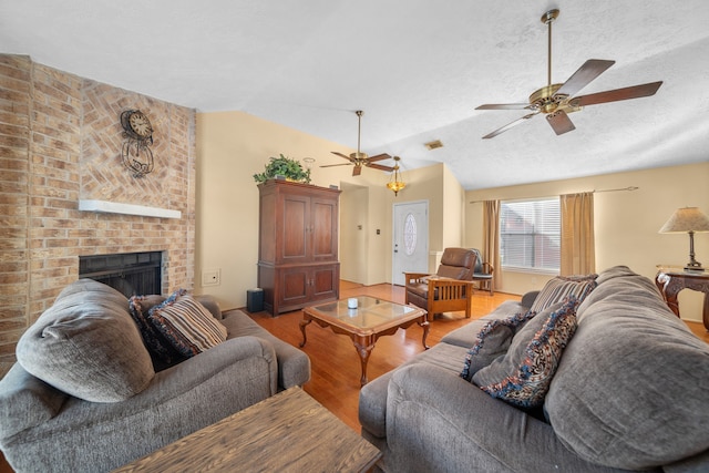 living room featuring a fireplace, lofted ceiling, hardwood / wood-style flooring, ceiling fan, and a textured ceiling