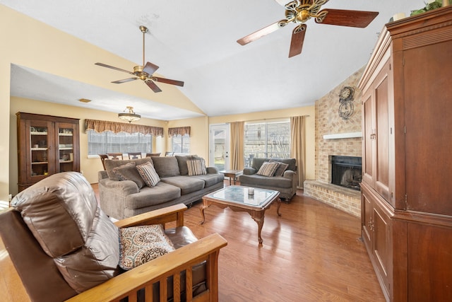 living room featuring vaulted ceiling, a brick fireplace, ceiling fan, and light wood-type flooring