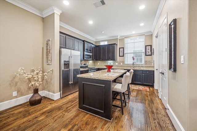 kitchen with crown molding, a kitchen breakfast bar, stainless steel appliances, a center island, and light stone counters