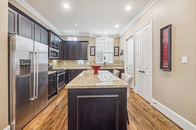 kitchen featuring ornamental molding, appliances with stainless steel finishes, light stone countertops, and a kitchen island