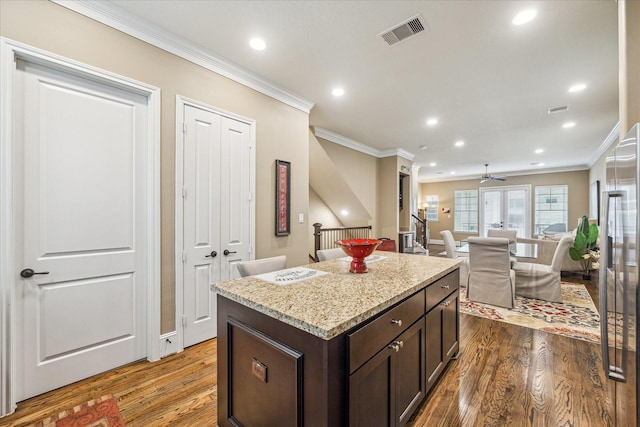 kitchen with crown molding, a kitchen island, dark wood-type flooring, and dark brown cabinetry