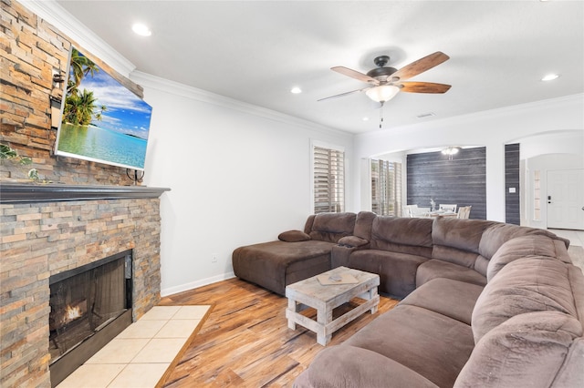 living room with crown molding, a stone fireplace, and light hardwood / wood-style flooring