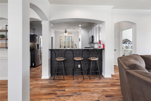 kitchen with ornamental molding, dark wood-type flooring, a breakfast bar area, and stainless steel fridge