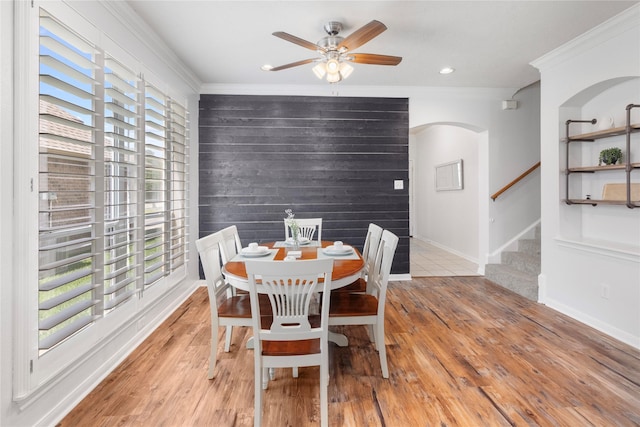 dining room featuring crown molding, ceiling fan, wooden walls, and light wood-type flooring