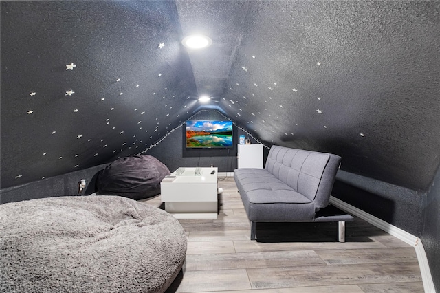 home theater room with lofted ceiling, light hardwood / wood-style floors, and a textured ceiling