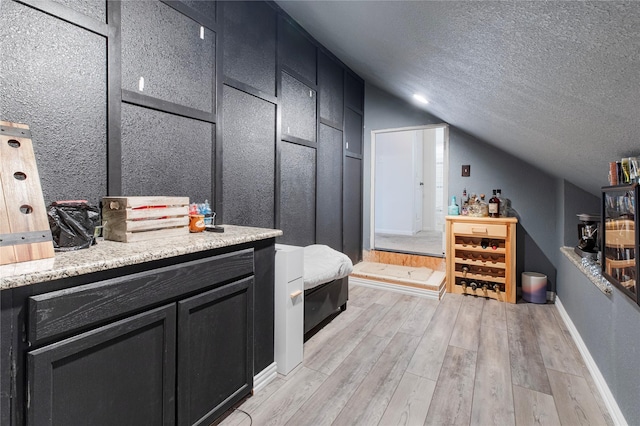 bathroom with wood-type flooring, lofted ceiling, vanity, and a textured ceiling