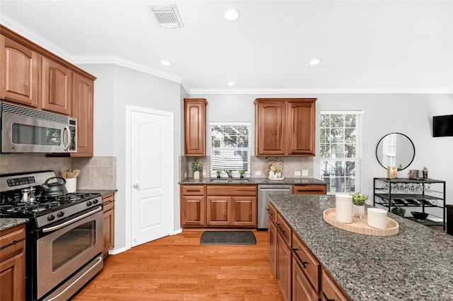 kitchen with sink, light wood-type flooring, ornamental molding, appliances with stainless steel finishes, and dark stone counters