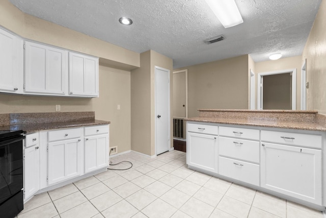 kitchen with light tile patterned floors, a textured ceiling, white cabinets, and range