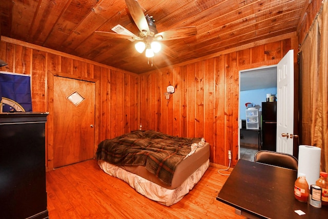 bedroom with wooden ceiling, wood finished floors, freestanding refrigerator, and wood walls