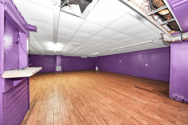 basement featuring a drop ceiling, visible vents, and wood finished floors