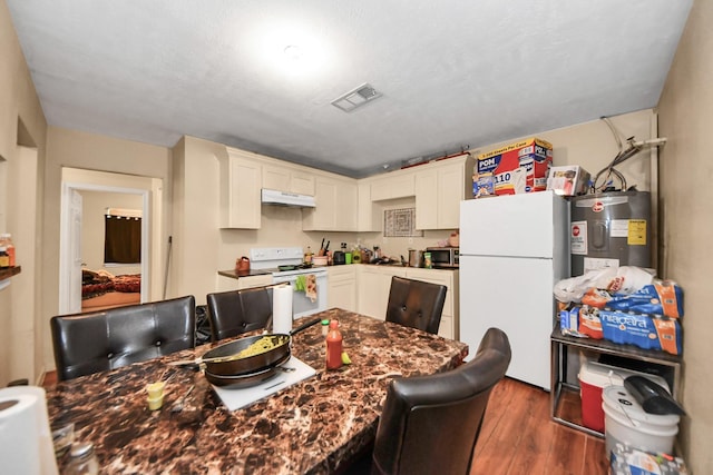 kitchen featuring visible vents, under cabinet range hood, water heater, dark wood-style floors, and white appliances