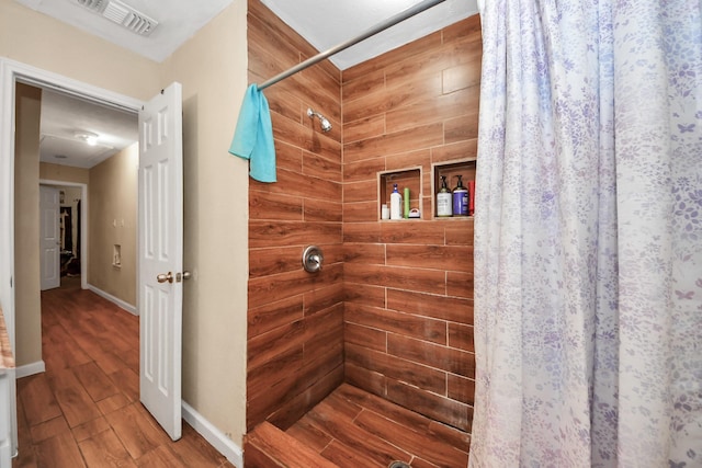 full bathroom featuring visible vents, tiled shower, baseboards, and wood finished floors