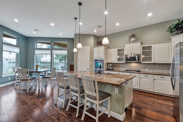 kitchen featuring pendant lighting, stainless steel appliances, light stone countertops, a kitchen island with sink, and white cabinets