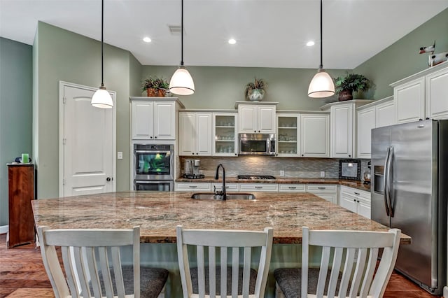 kitchen with pendant lighting, stainless steel appliances, a kitchen island with sink, and sink