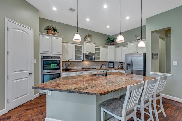 kitchen with stainless steel appliances, decorative light fixtures, sink, and a center island with sink