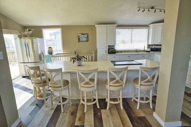 kitchen with a breakfast bar area, appliances with stainless steel finishes, dark hardwood / wood-style floors, a wealth of natural light, and white cabinets