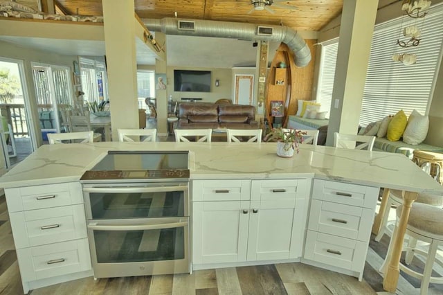 kitchen with white cabinets, a kitchen bar, double oven range, light stone counters, and wood ceiling