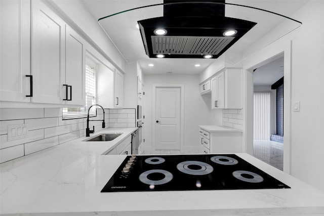 kitchen with sink, white cabinetry, island range hood, light stone countertops, and backsplash