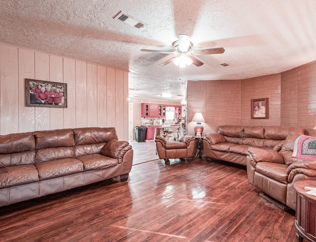 living room with ceiling fan, brick wall, a textured ceiling, and dark hardwood / wood-style flooring