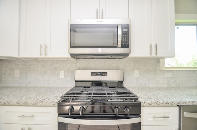 kitchen with white cabinetry, backsplash, light stone countertops, and gas range oven