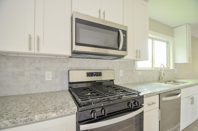 kitchen with stainless steel appliances, white cabinetry, sink, and light stone counters