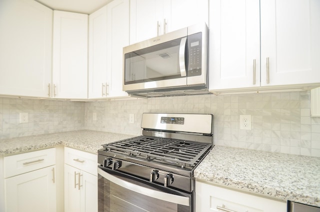 kitchen with stainless steel appliances, white cabinetry, and light stone countertops