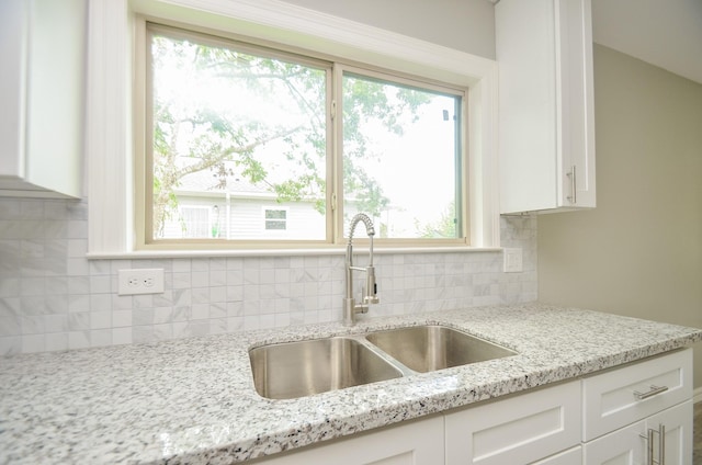 kitchen featuring light stone counters, sink, backsplash, and white cabinets