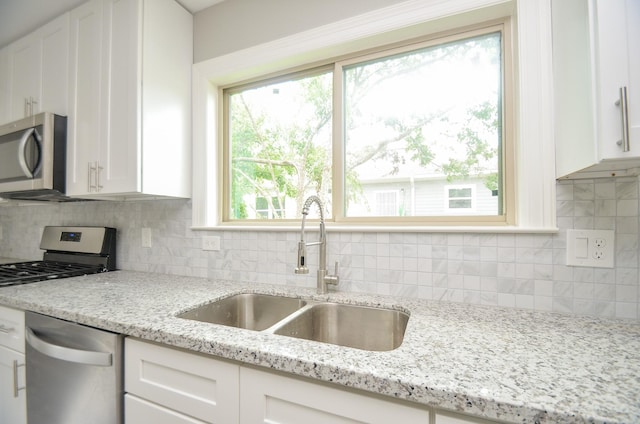 kitchen with white cabinetry, stainless steel appliances, light stone countertops, and sink