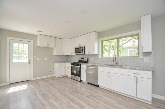 kitchen with white cabinetry, sink, stainless steel appliances, and light stone countertops