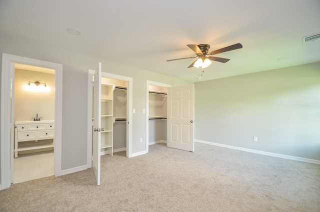 unfurnished bedroom featuring light carpet, two closets, and ceiling fan