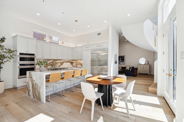 kitchen with light wood finished floors, stainless steel appliances, a high ceiling, and visible vents