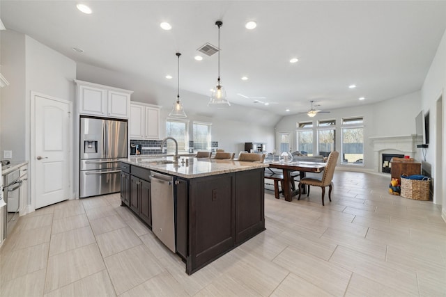 kitchen with decorative light fixtures, an island with sink, white cabinets, light stone counters, and stainless steel appliances