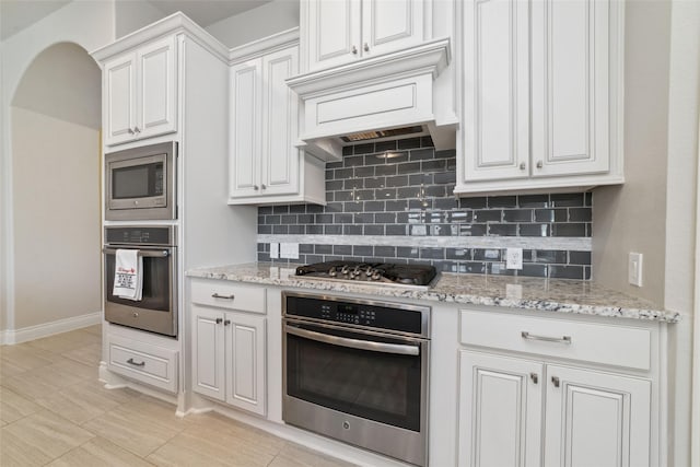 kitchen with white cabinetry, appliances with stainless steel finishes, decorative backsplash, and premium range hood