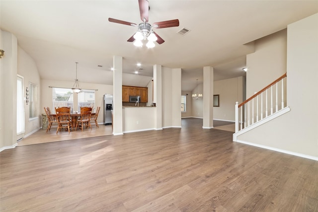 unfurnished living room with ceiling fan with notable chandelier, vaulted ceiling, and light wood-type flooring