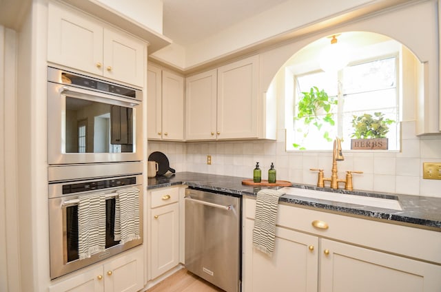 kitchen featuring sink, appliances with stainless steel finishes, dark stone countertops, backsplash, and light wood-type flooring