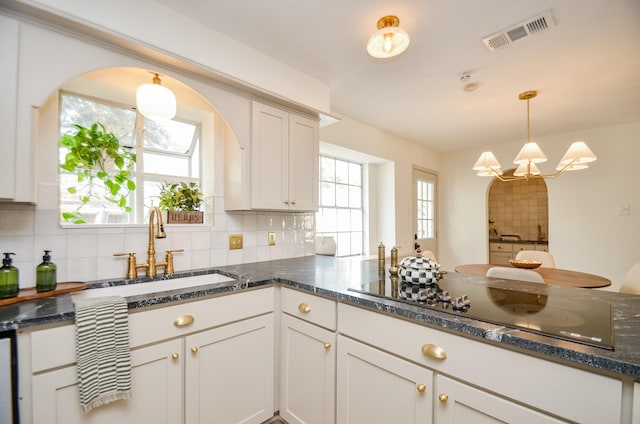 kitchen with sink, decorative light fixtures, white cabinets, black electric stovetop, and backsplash