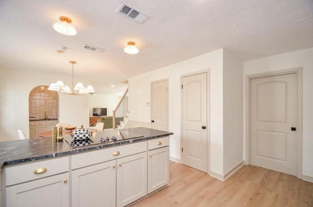 kitchen with pendant lighting, dark stone countertops, white cabinets, black electric cooktop, and light wood-type flooring