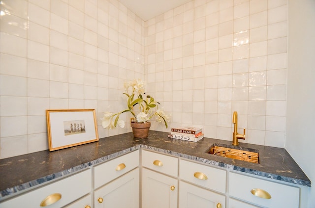 kitchen with sink, tile walls, white cabinets, dark stone counters, and backsplash