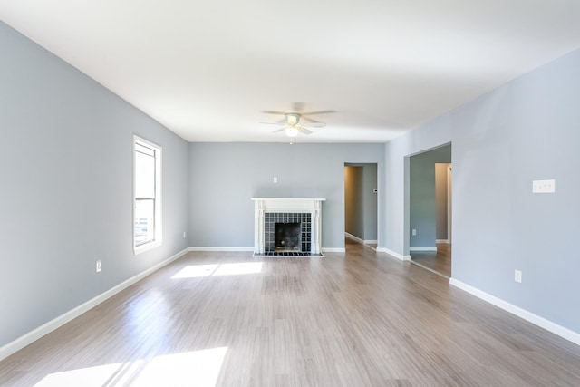 unfurnished living room with a tiled fireplace, light hardwood / wood-style flooring, and ceiling fan